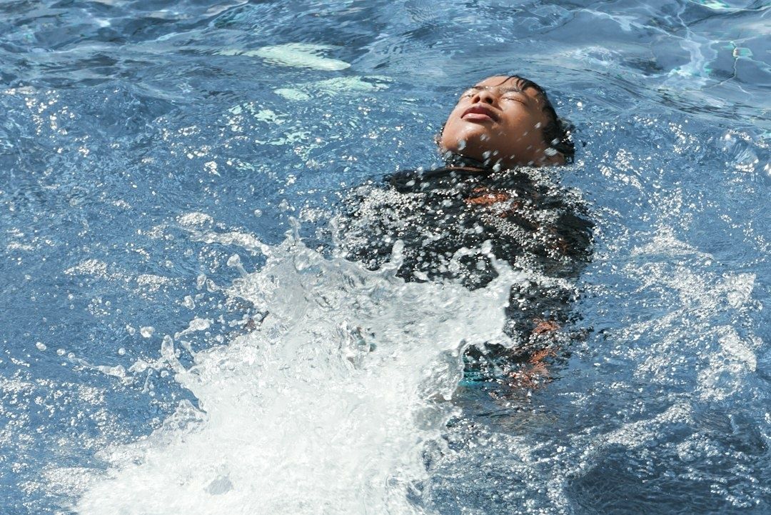 Person in dark clothing splashing backward in a swimming pool