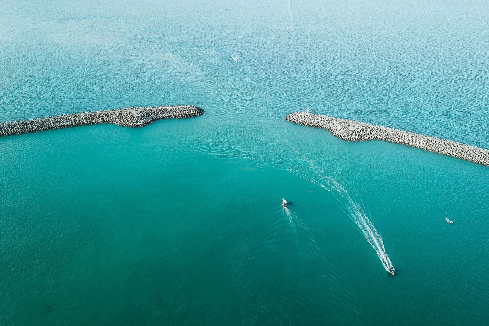 Boats pass between two concrete breakwaters in turquoise water