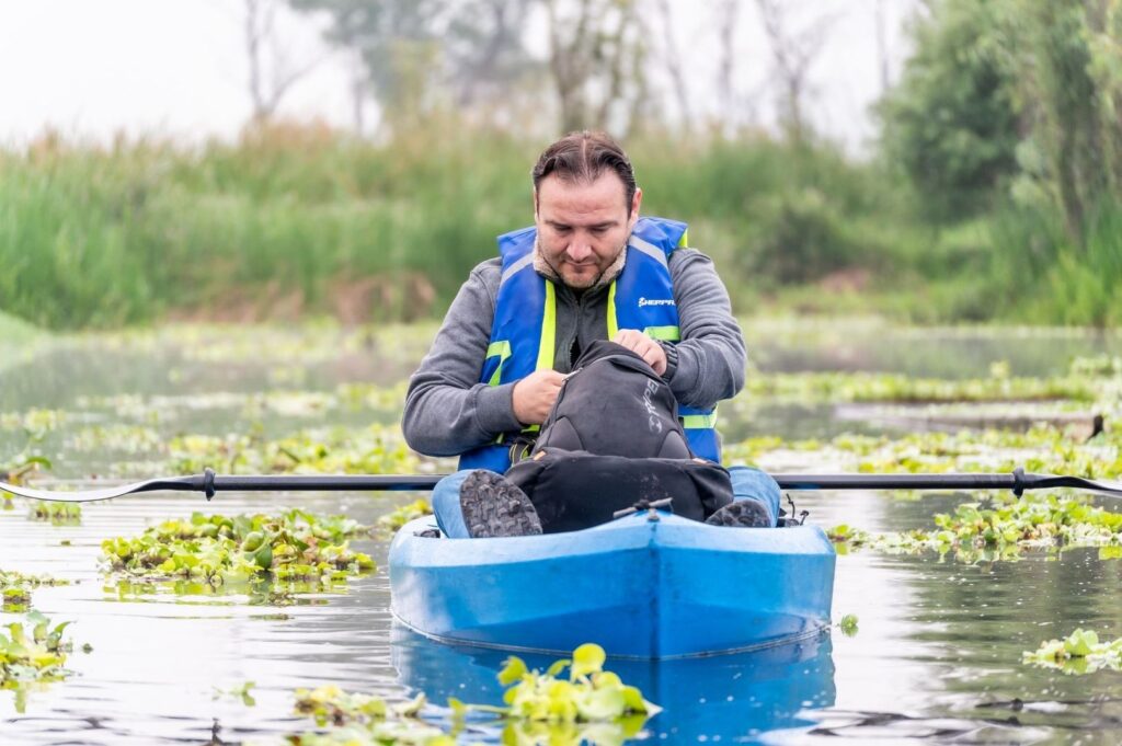 Man in a kayak wearing a life vest among aquatic plants