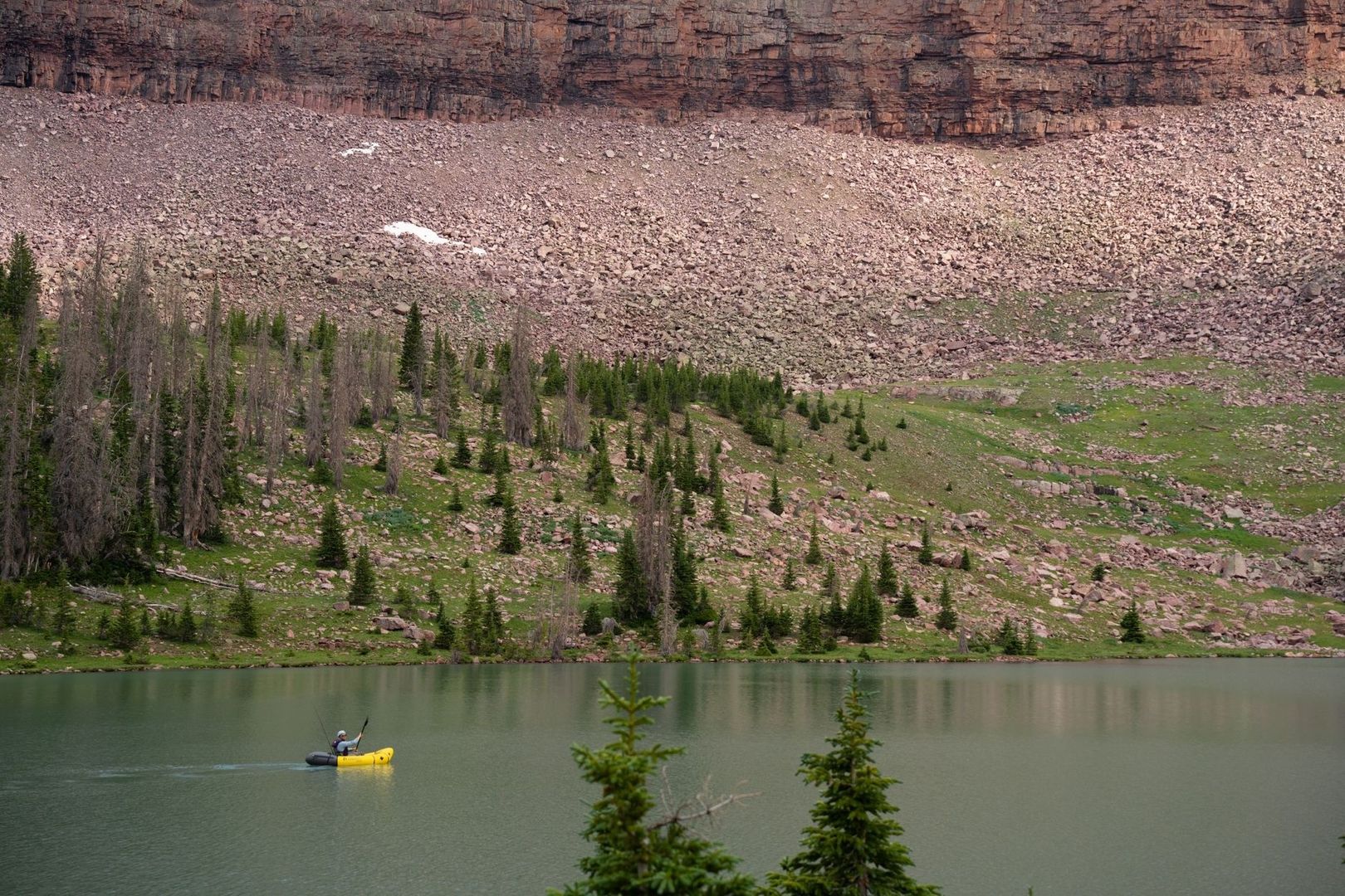 Paddler in a yellow packraft on a mountain lake below cliffs